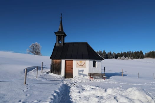 Little chapel nestled in a winter wonderland on a sunny day, Kapelle Mariä Heimsuchung, Wertach, Allgäu, Bavaria, Germany 2022