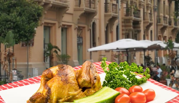 Grilled fresh fried chicken with vegetables on a white plate on table with red checkered table cloth over a blurred restaurant background. Meat on barbecue grill.