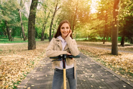 Young beautiful stylish woman riding electric scooter in autumn park, ecological transport
