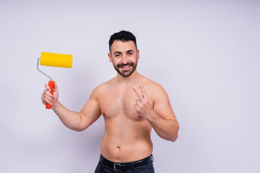 Cheerful young topless man hold paint roller isolated on a grey background studio.