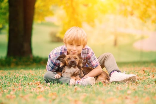 Boy hugging a dog and plyaing with in the fall, city park