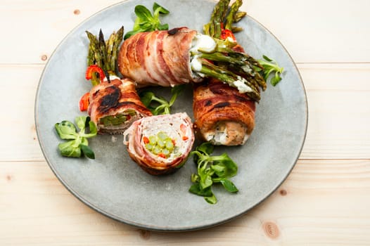 Roast meat rolls stuffed with green young asparagus on wooden table.