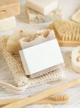 Organic handmade beige soap bar with blank label on soap saver bag near hygiene Items - natural sponges and brush, bamboo toothbrushes and cotton swabs, close up, mockup