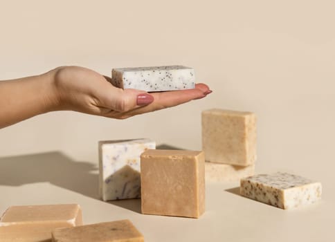 Hand keeps natural beige soap bars with blank label on light beige, close up, hard shadows. Hygiene products for Spa and skin care. Using organic handmade soap in everyday routine