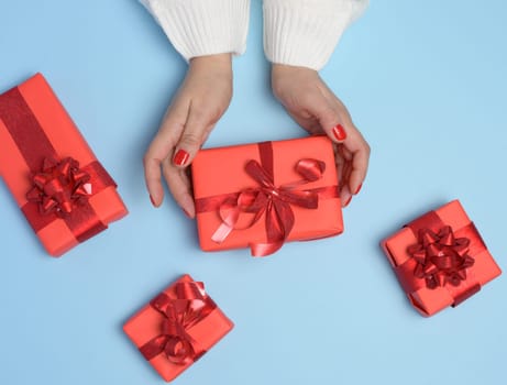 Female hands holding a gift box with a red ribbon on a blue background. View from above