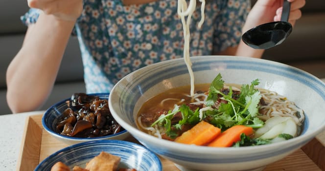 Woman eat taiwanese braised beef noodles bowl in restaurant
