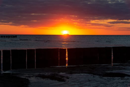 Beautiful orange sunset over the sea, a ship on the horizon, with wood groynes