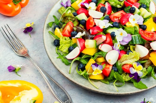 Spring salad of fresh vegetables decorated with edible flowers. Top view.