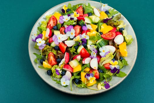 Spring salad of fresh vegetables decorated with edible flowers. Top view.