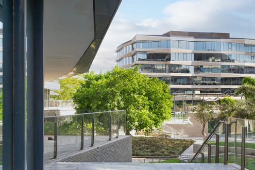 Contemporary urban city district with well run glass building and verdant lawn and trees before sunset