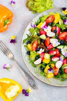 Spring salad of fresh vegetables decorated with edible flowers. Top view.
