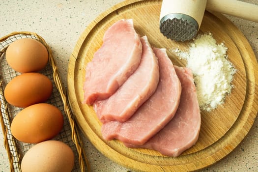 Sliced pork loin on a board, flour and eggs, top view