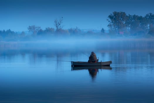 Angler in a boat and fog on a calm blue lake