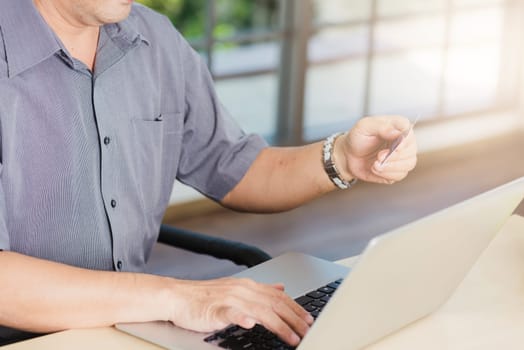 Closeup Asian senior adult man holding credit card and using technology on laptop computer, Online shopping payment with a customer network connection via an Omnichannel system