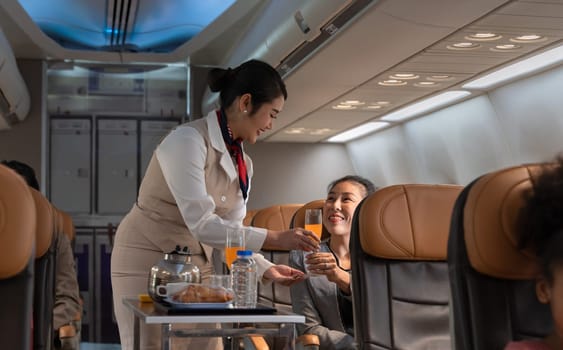 Air hostess or cabin crew working in airplane. Female flight attendant serving orange juice to businesswoman passenger on board. Airline transportation and tourism concept.