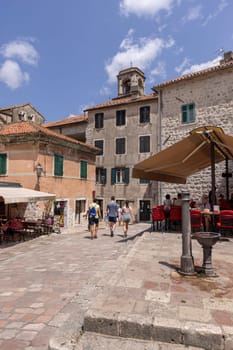 Kotor, Montenegro - June 26, 2023:  Picturesque small square in the Old Town, surrounded by stone tenement houses, with outside restaurants and old metal well, Kotor, Montenegro