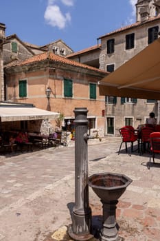 Kotor, Montenegro - June 26, 2023:  Picturesque small square in the Old Town, surrounded by stone tenement houses, with outside restaurants and metal well, Kotor, Montenegro