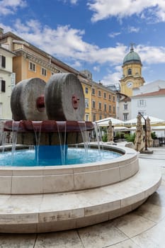 Rijeka, Croatia - September 23, 2023: Kobler Square Fountain with modern water-fountain. Baroque city clock tower in a distance