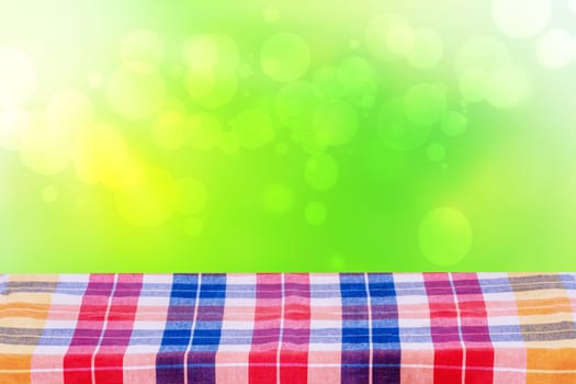 Empty table product. Empty colorful checkered tablecloth over abstract blurred natural green background texture with space for food and product display montage.