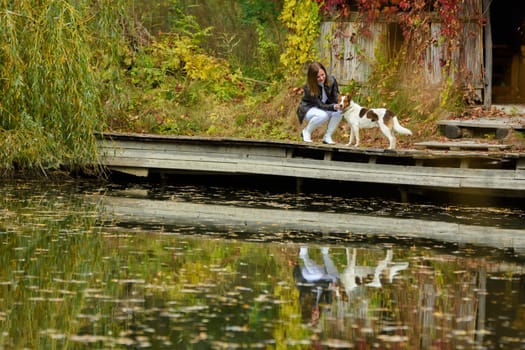 Young beautiful girl petting a dog near a lake in an autumn park