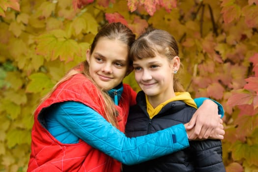 Close-up portrait of two girls of Slavic appearance in casual autumn clothes against the backdrop of an autumn forest, children looking to the left