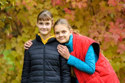 Portrait of two girls of Slavic appearance in casual autumn clothes against the background of an autumn forest