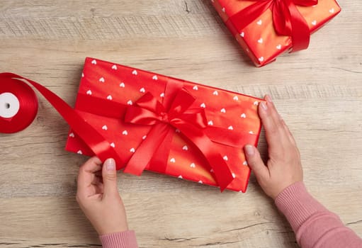 Female hands holding a gift box with a red ribbon on a brown background. View from above