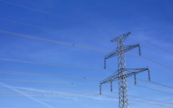 Looking up to steel electricity pylon against blue sky with only few clouds streaks