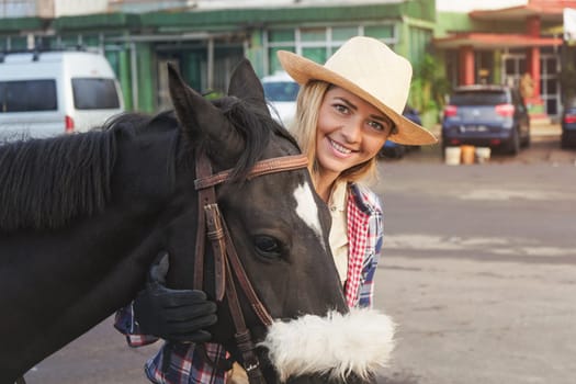 Young woman in straw hat standing behind dark brown horse, smiling, detail on their faces, city buildings in background