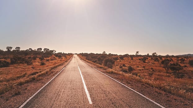 Legendary RN7 - stands for Route Nationale - road going through wild African savanna with small trees and bushes at sides, sun shines in background, typical scenery of region near Ilakaka