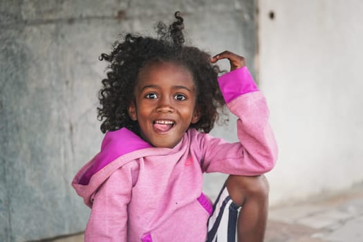 Ranohira, Madagascar - April 29, 2019: Small girl in pink sweatshirt smiling into camera with her tongue our. People in Madagascar, especially Malagasy children are poor but cheerful.