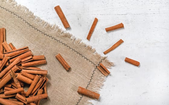 Tabletop view - Heap of cinnamon bark sticks on linen tablecloth and white stone desk