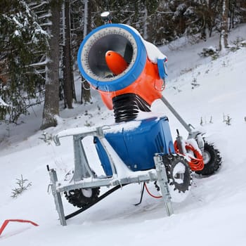 Bright orange and blue snow making cannon, trees in background