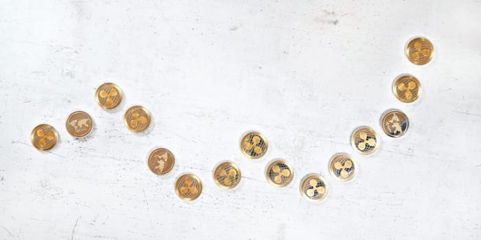 Top down view, white stone board desk with golden ripple coins in shape of rising graph - bullish XRP cryptocurrency market illustration