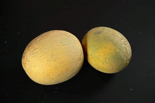 Two yellow Cantaloupe melons on black marble like board