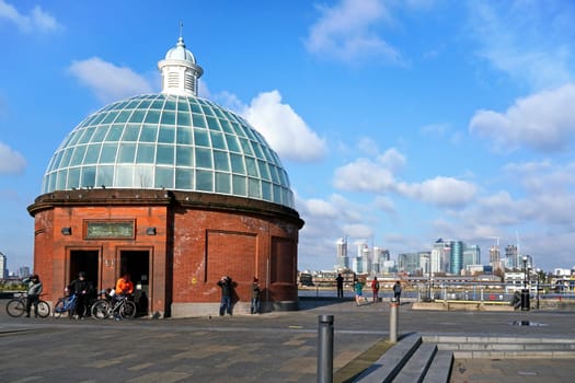 London, United Kingdom - February 02, 2019: Group of cyclists entering Greenwich foot tunnel under river Thames on sunny day, river and Canary Wharf district in background