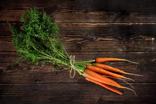 Bunch of carrots with leaves on dark wooden board, view from above