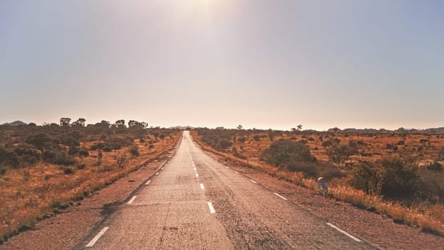 Legendary RN7 - stands for Route Nationale - road going through wild red African savanna with small trees and bushes on sides, at region near Ilakaka, sun shines in background