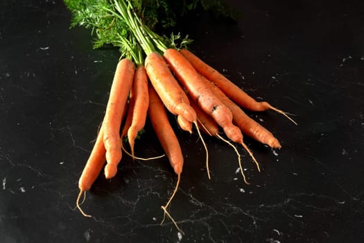 Bunch of organic raw carrot with green leaves on black marble like board, view from above