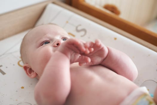 4 months old infant baby boy on changing table, detail on his face, partly hidden behind arms