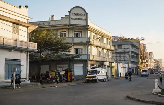 Fianarantsoa, Madagascar - May 06, 2019: Typical morning scene - town street, young girls in uniforms walking to school, cars coming on road from distance, sun shines on buildings mostly hotels.