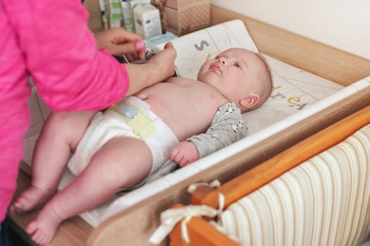 4 months old infant baby boy, at changing table, his mother putting clothes on
