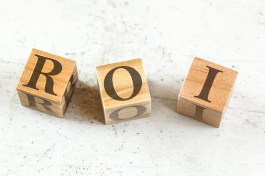 Three wooden cubes with letters ROI (stands for Return on Investment) on white board.