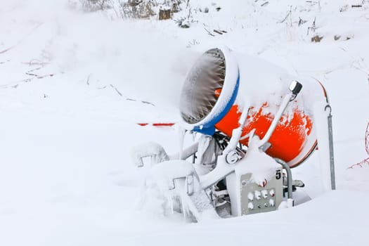 Bright orange snow cannon spraying ice crystals over ski piste, close up detail