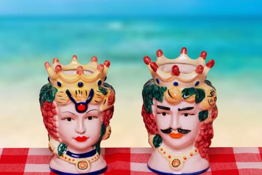 Souvenir from Sicily. Traditional sicilian ceramic pots or vases with heads of a couple of lovers of Moorish heads on red checked napkin over abstract ocean background.