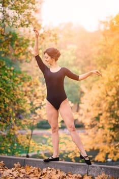 Beautiful female, ballerina, athlete in black bodysuit training in park