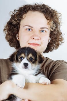 Close-up portrait of face of charming woman, owner of small Welsh corgi puppy, whom she holds in her arms. Dog food. Pets. Dog in family. Features of keeping puppies. Veterinary control. Loyal friend.