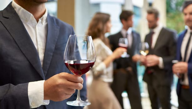 Businessman holding a glass of red wine in the office with colleagues in the background. AI generated