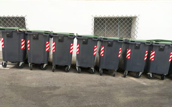 Line of grey dumpsters braking on slope. Urban background