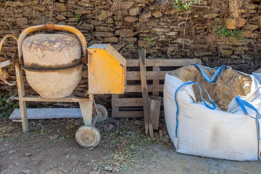 Raffia large sand sack stacked close to cement mixer. Rural residences construction industry concept